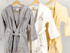 Three bathrobes in gray, white, and yellow hanging on a rack against a light gray background.