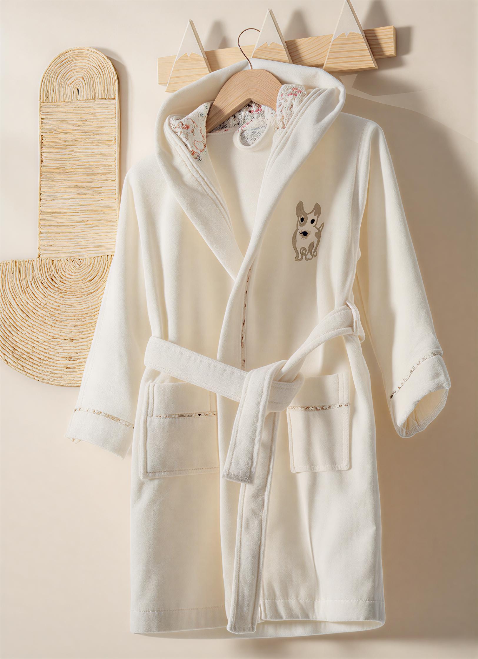 White robe with dog embroidery on a wooden hanger against a beige wall.