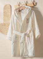 White robe with dog embroidery on a wooden hanger against a beige wall.