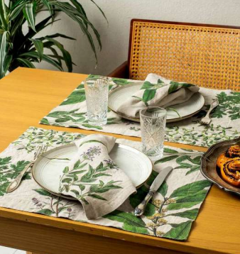 Dining table set with green leaf-patterned placemats, plates, and glasses.