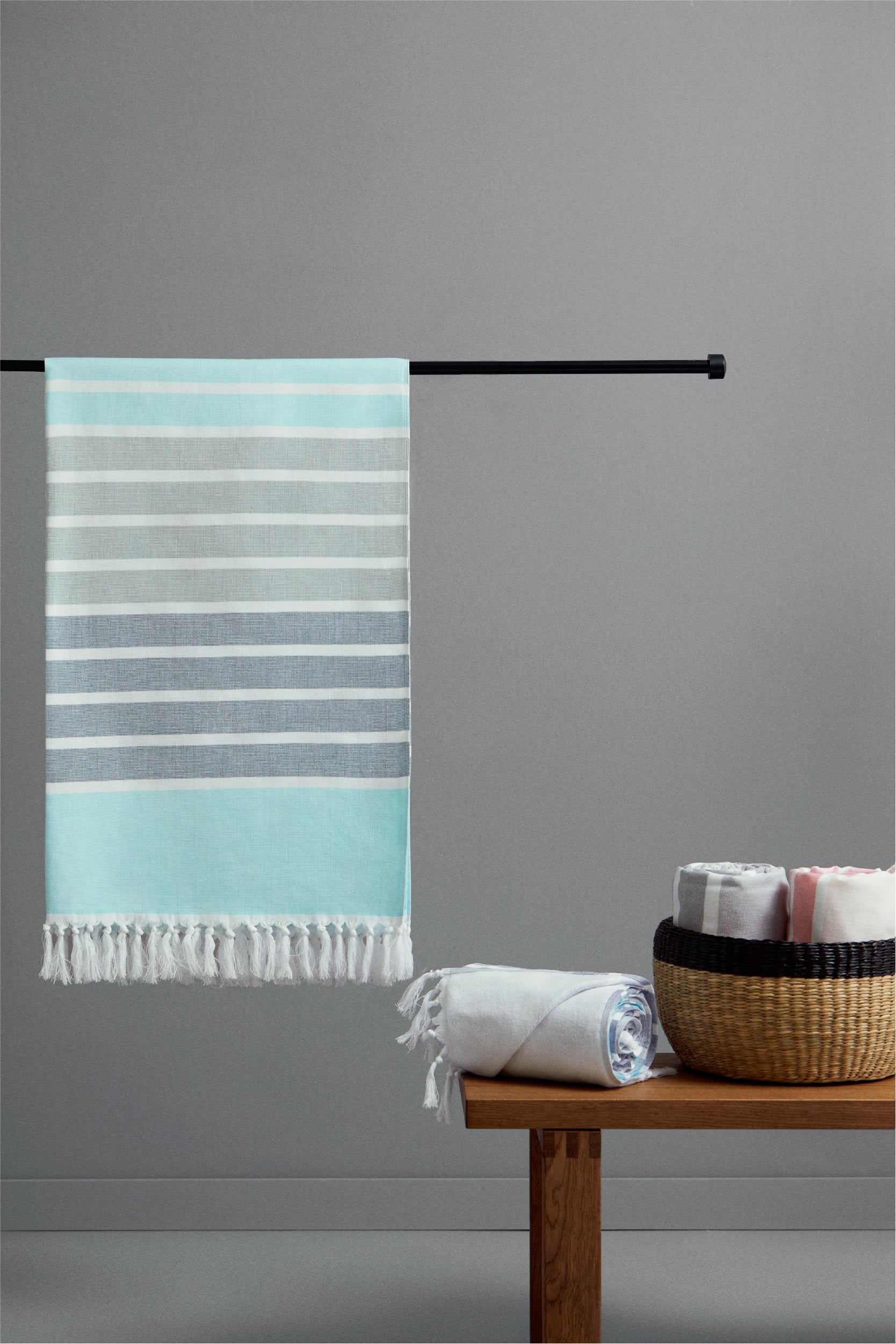 Striped towel hanging on a rod with additional towels on a wooden table against a gray wall.