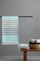 Striped towel hanging on a rod with additional towels on a wooden table against a gray wall.