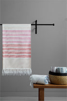Striped towel hanging on a rack with a wooden table and basket in the foreground against a gray wall.