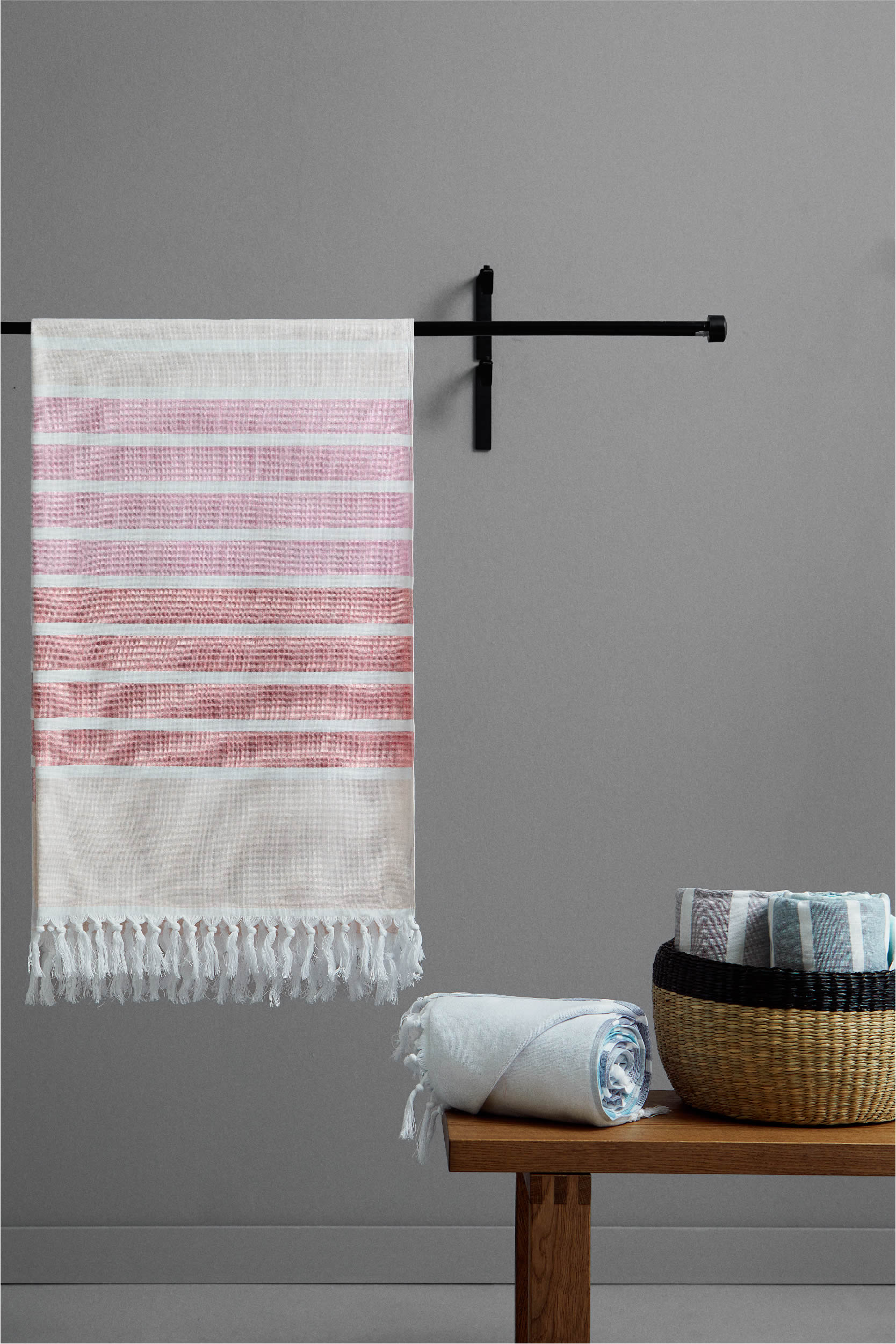 Striped towel hanging on a rack with a wooden table and basket in the foreground against a gray wall.