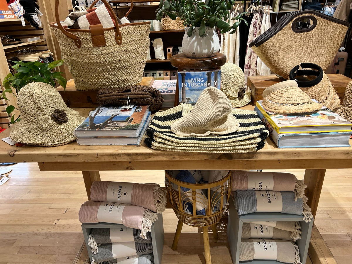 Display of hats, bags, and books on a wooden table in a store setting.