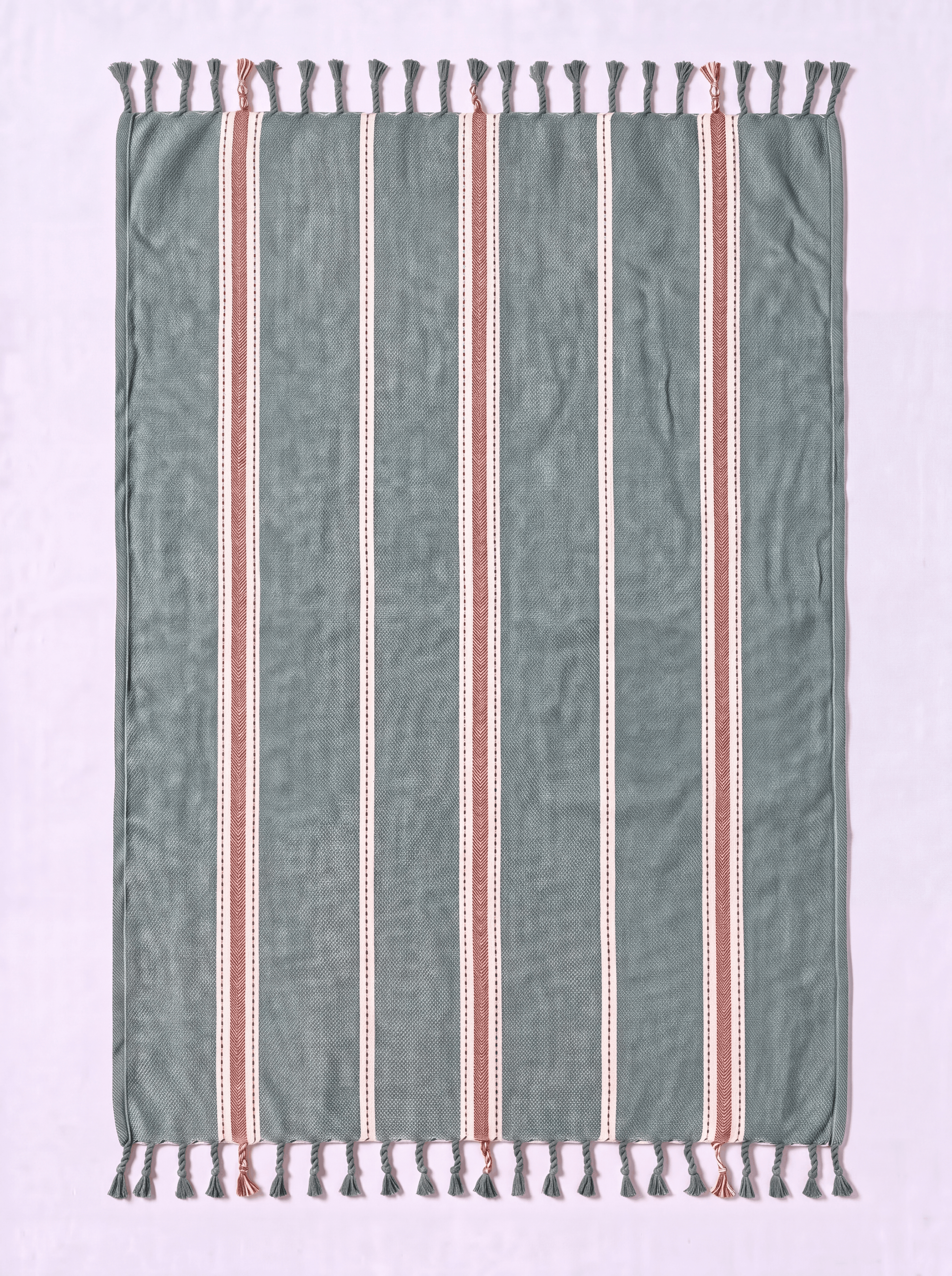 A rectangular woven towel with fringe tassels on both ends, featuring a muted sage green base with vertical stripes in white and terracotta red.