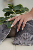  Zeus Organic Cotton Bath, Hand & Washcloth Set in Cozy Cobalt, with a woman’s hand gently holding the towels, accompanied by a plant, highlighting the soft texture, vibrant colour, and natural aesthetic