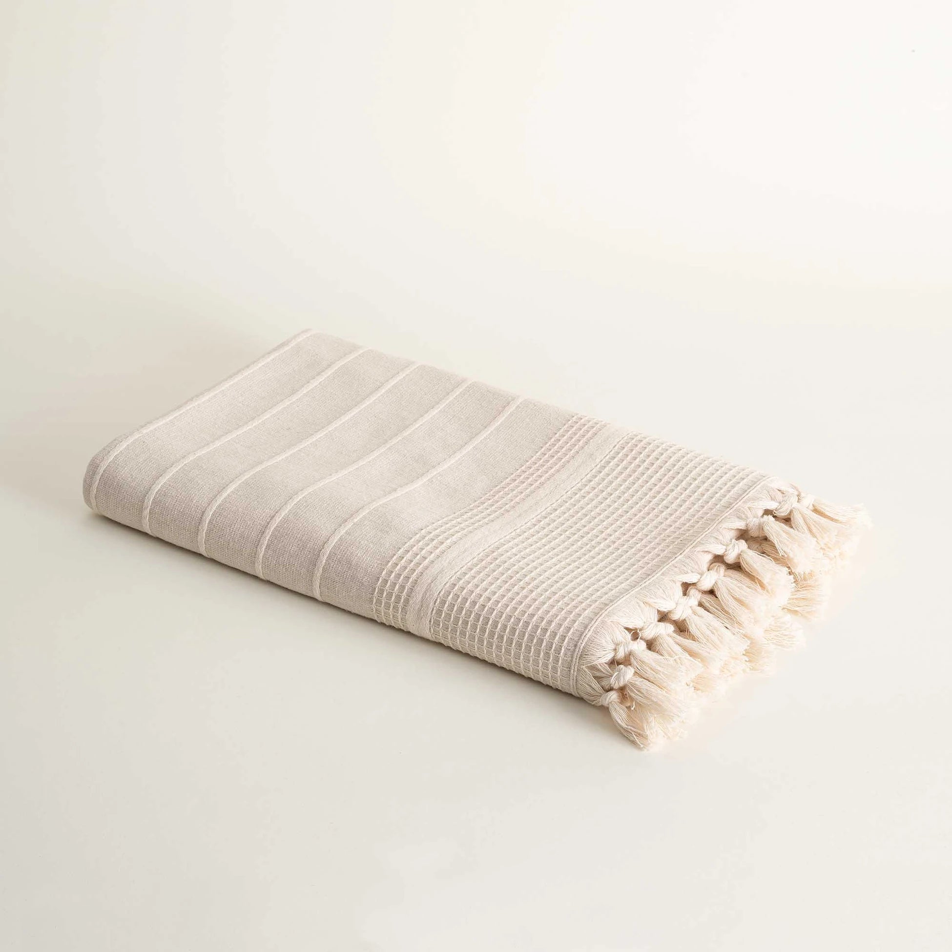 Folded Arden Hemp and Organic Cotton Bath Towel with tassels in sand and white highlighting the soft texture natural color and elegant tassel details of this luxury bath towel and organic bath towel