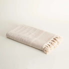 Beige striped towel with tassels on a light gray background