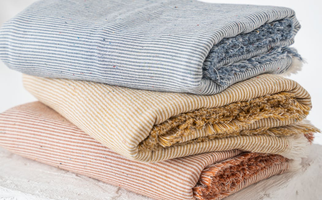 Stack of folded textured blankets in various colors on a light wooden surface