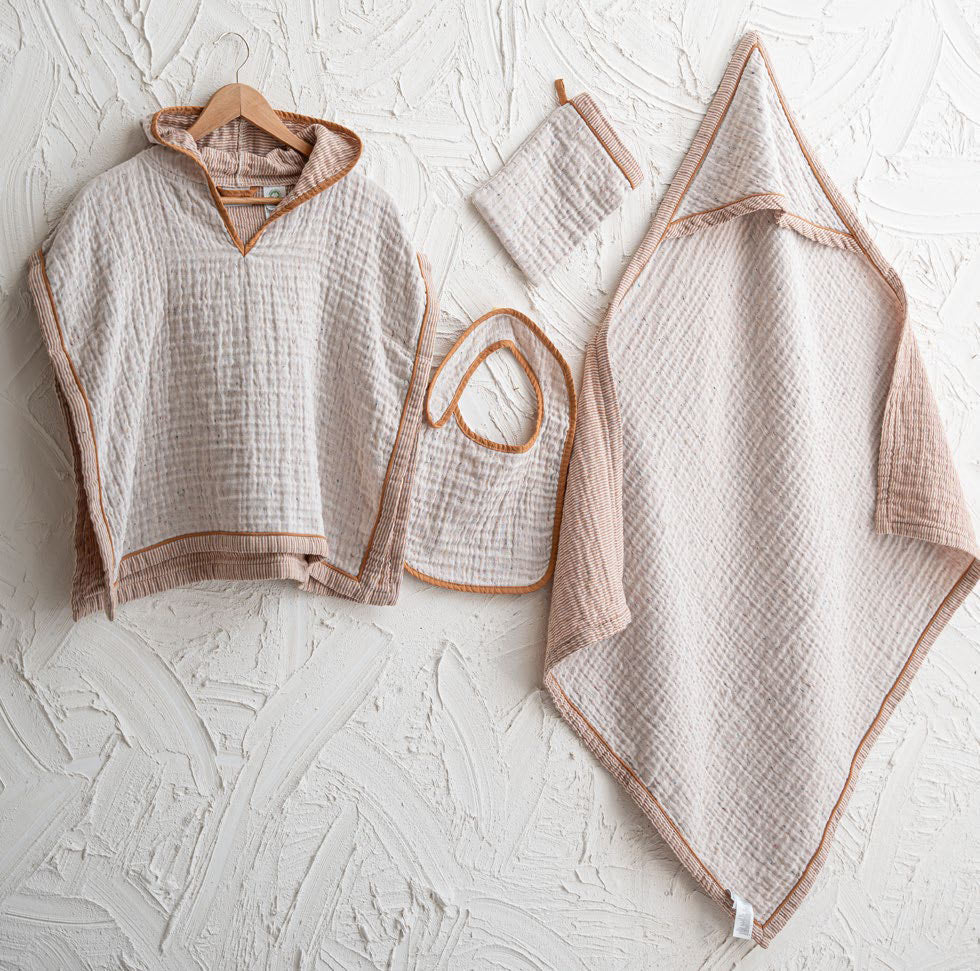 Baby clothing set including a poncho, bib, and blanket on a textured white surface.