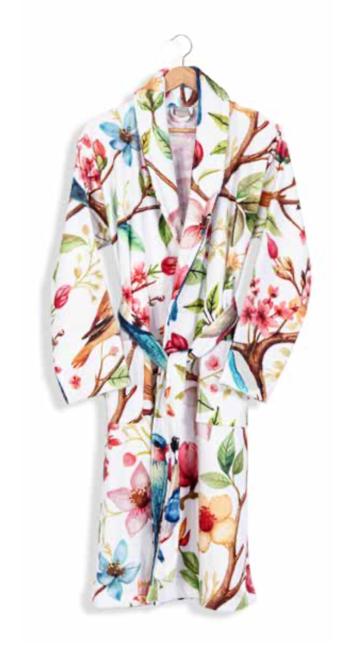 White bathrobe with colorful floral and bird print design hanging on wooden hanger — botanical-inspired sustainable home textile.