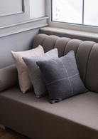 Talin collection decorative cushions in light and dark neutral tones with center-stitched detail, styled on a grey sofa — refined sustainable home decor with matching bed cover.