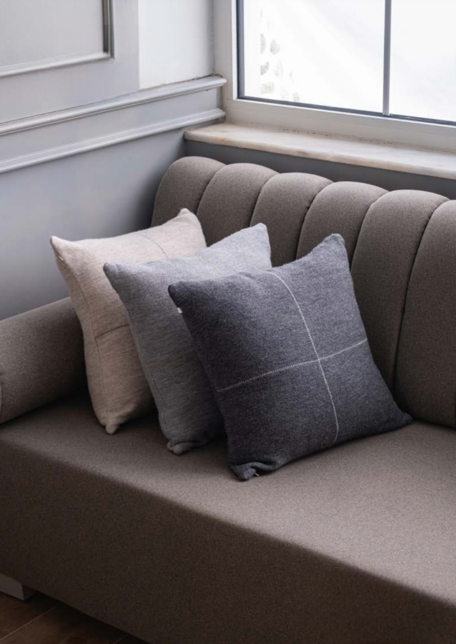Talin collection decorative cushions in light and dark neutral tones with center-stitched detail, styled on a grey sofa — refined sustainable home decor with matching bed cover.