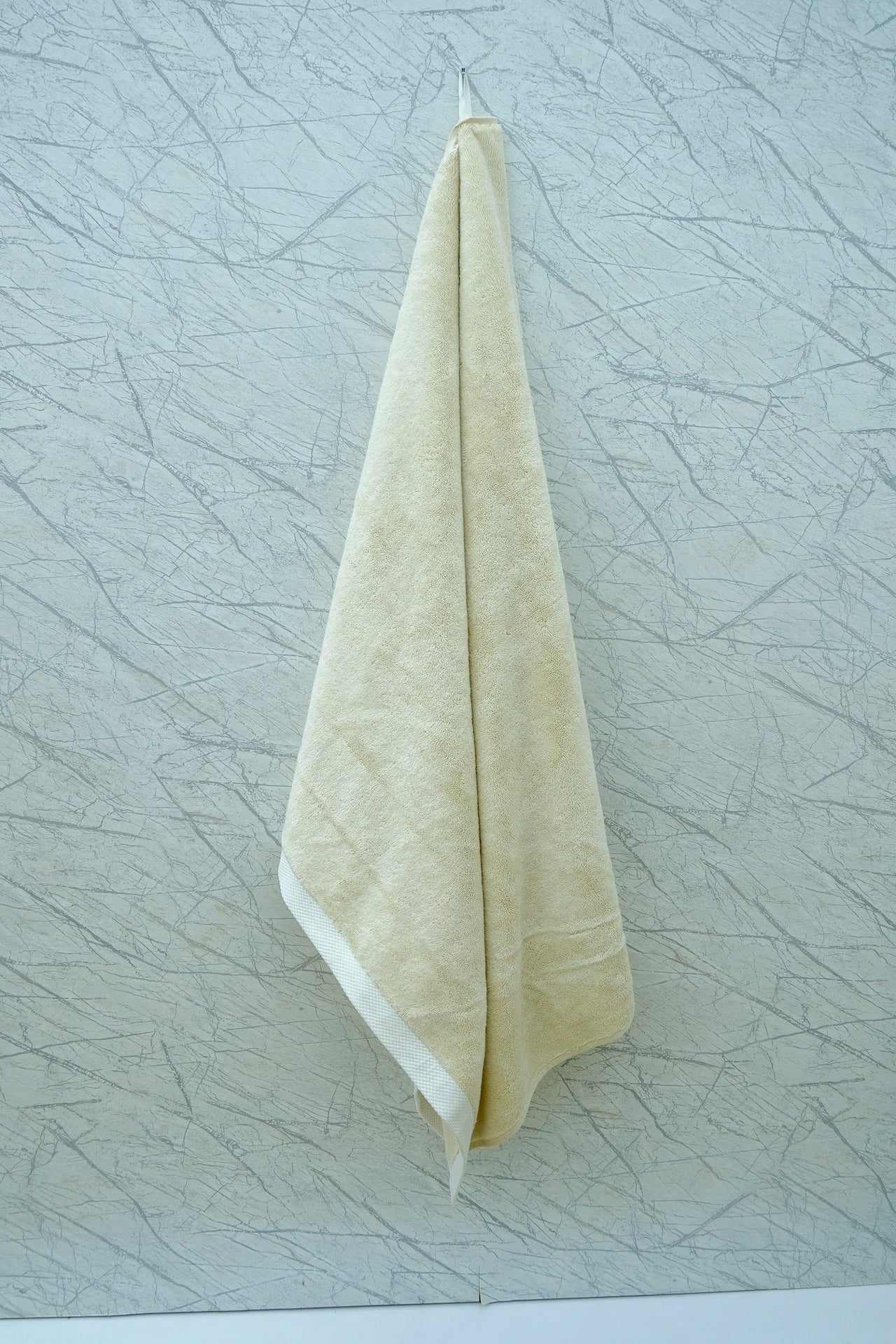 Cream-colored Minoa Home organic cotton hand towel hanging on a textured marble wall, showcasing spa-inspired bathroom decor.
