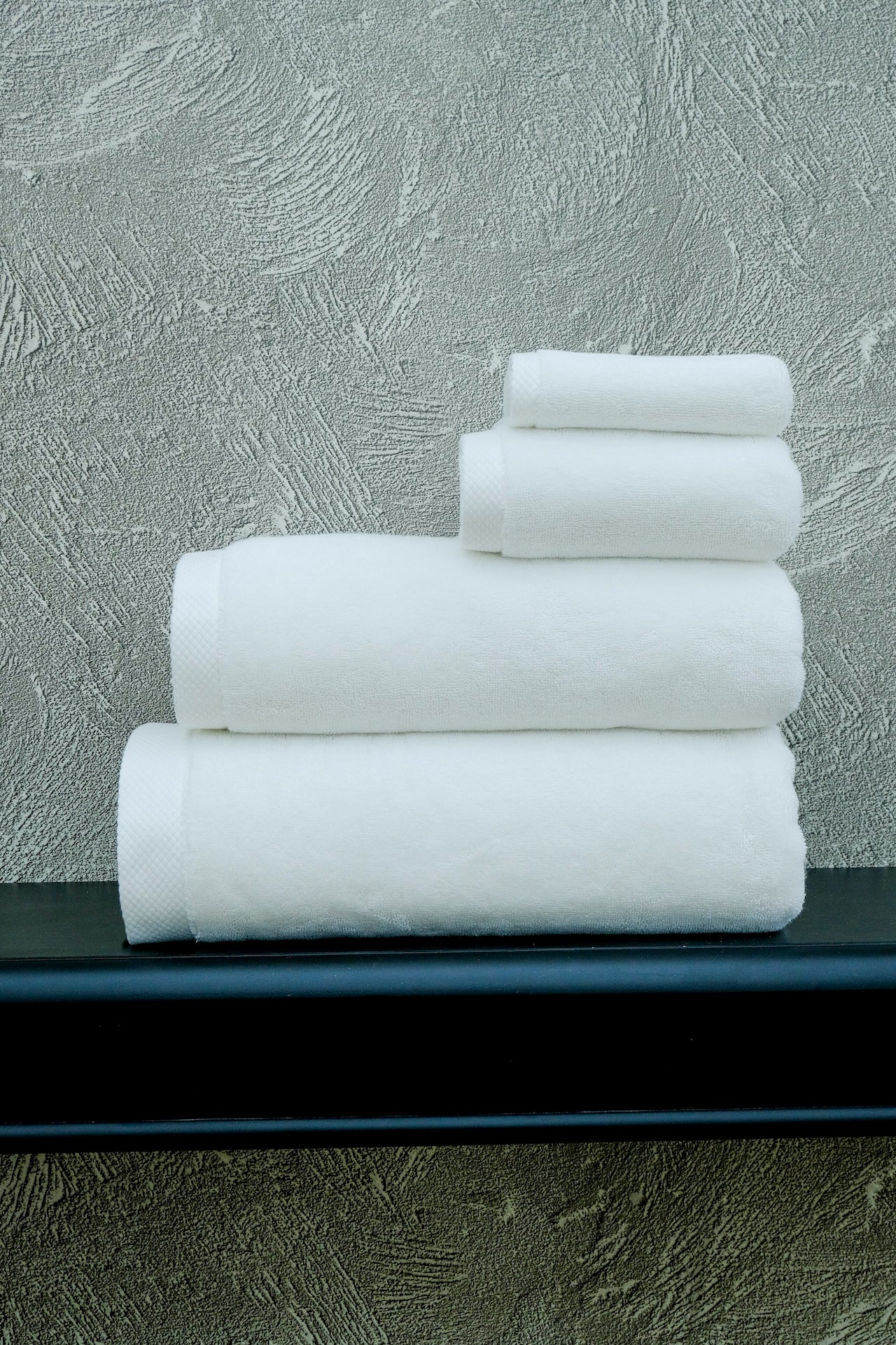 Stack of white towels on a black surface with a textured gray wall background