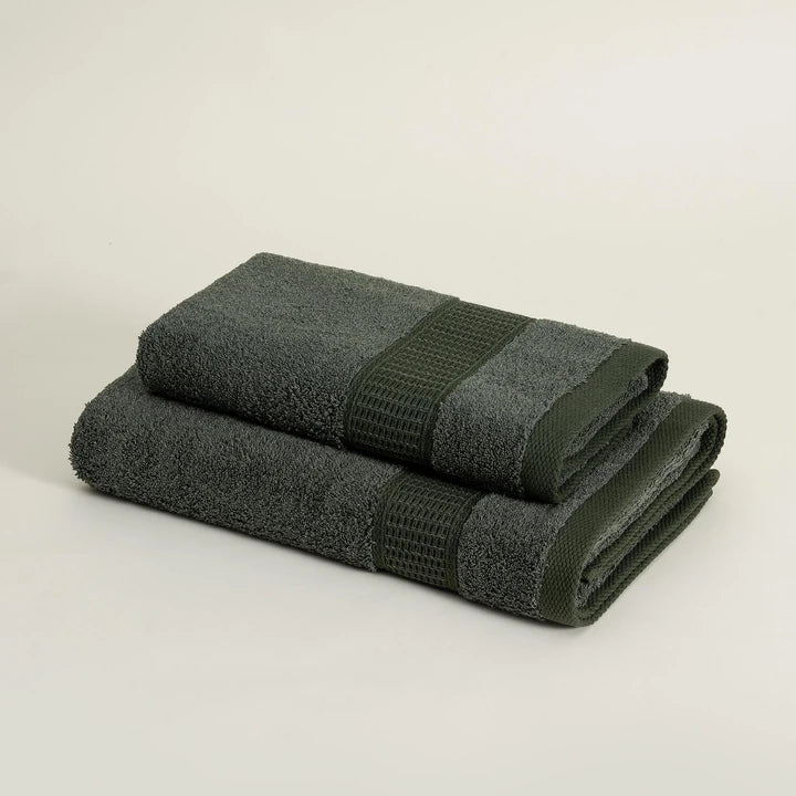 Two folded dark green towels on a light beige background