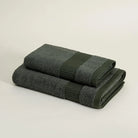 Two folded dark green towels on a light beige background