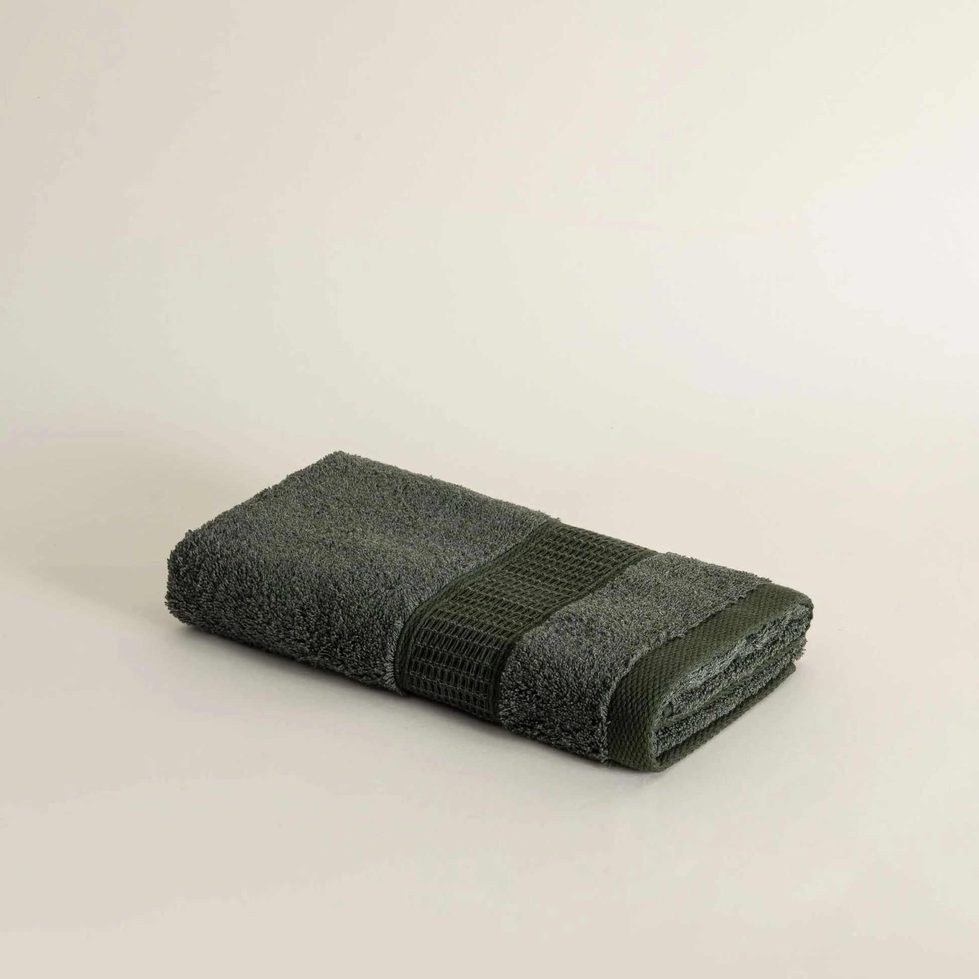 Folded dark green towel on a light beige background