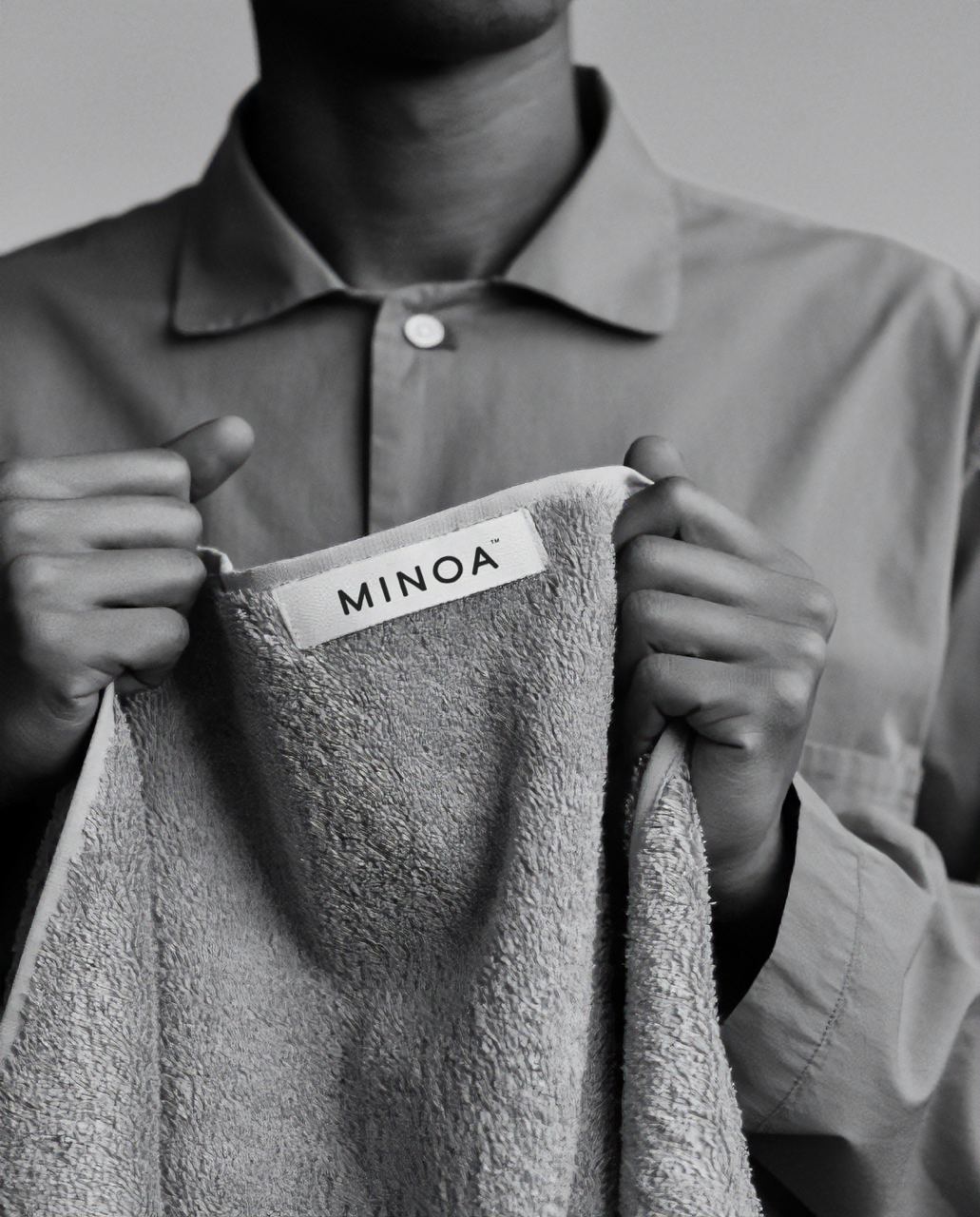 Person holding a towel with 'MINOA' label against a neutral background