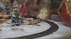 Red toy train on a snowy track with Christmas trees, ornaments, and warm holiday lighting in the background