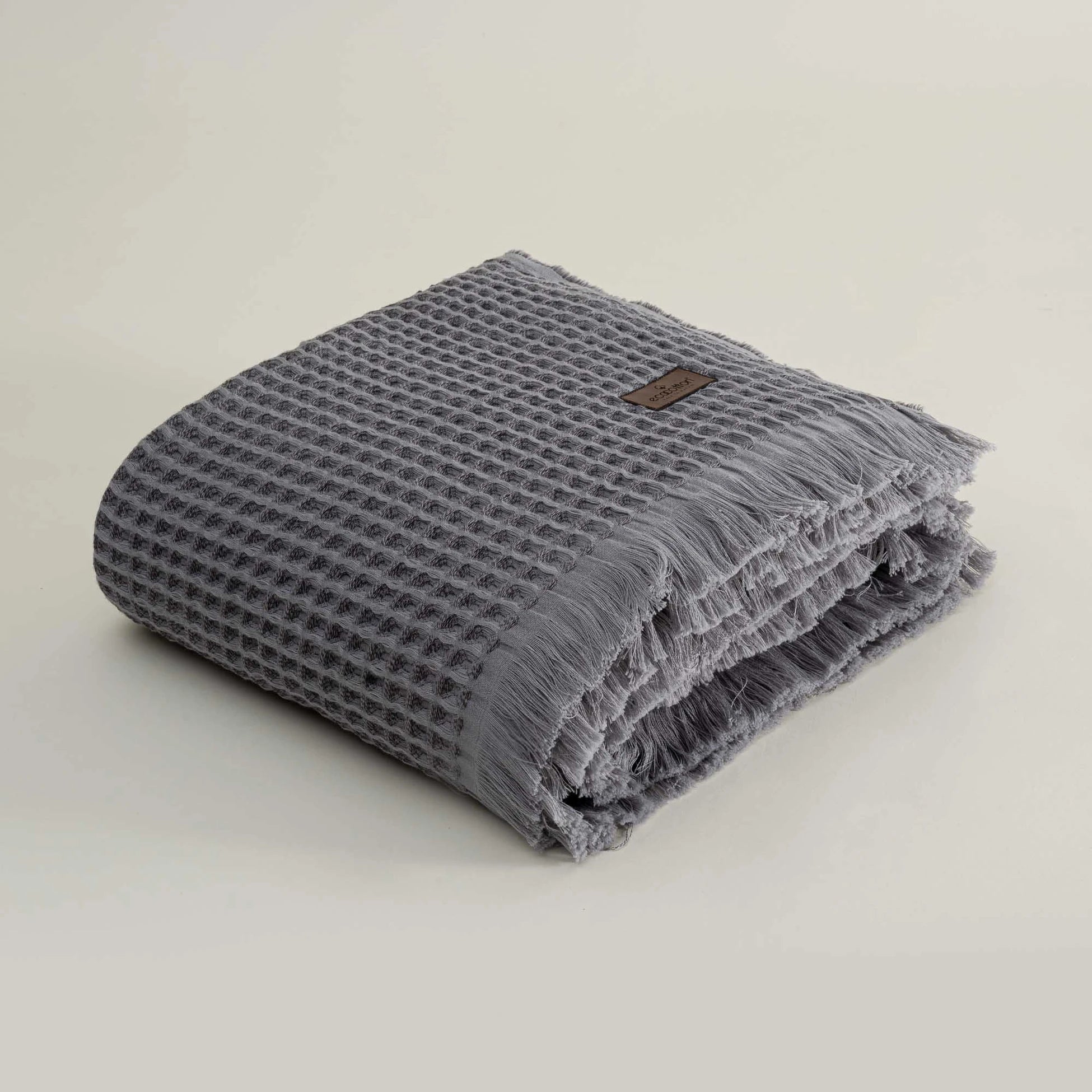 Folded gray textured towel with a brand label on a light beige background