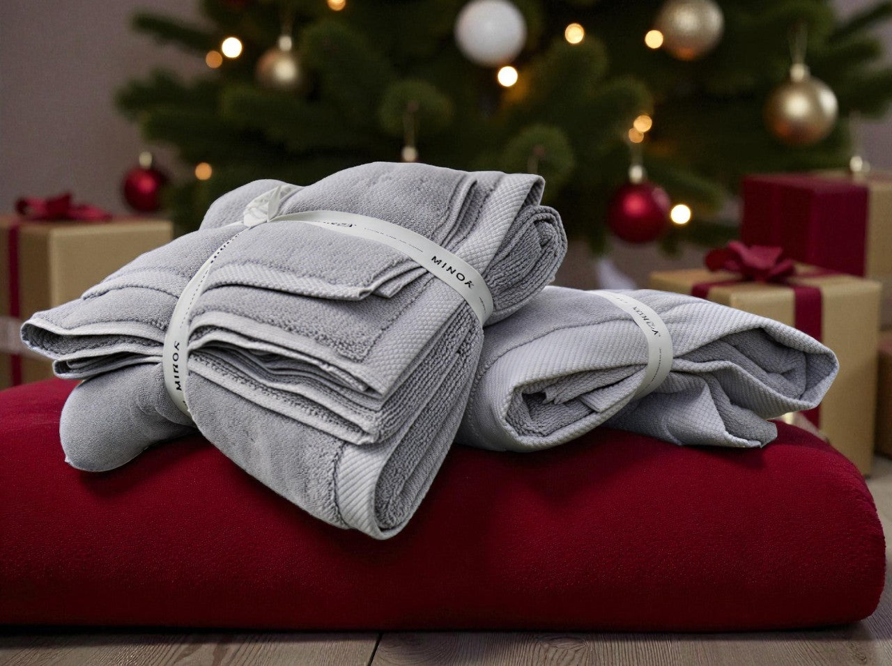 Stack of gray towels on a red surface with a decorated Christmas tree in the background